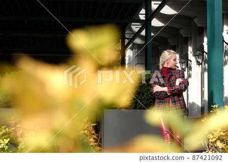 fashionable blonde girl with a red lipstick posing outdoors . Dressed in a red leather leggings, turtleneck and checkered jacket. fit figure fashionable blonde girl with a red lipstick posing outdoors . Dressed in a red leather leggings, turtleneck and checkered jacket. fit figure 87421092