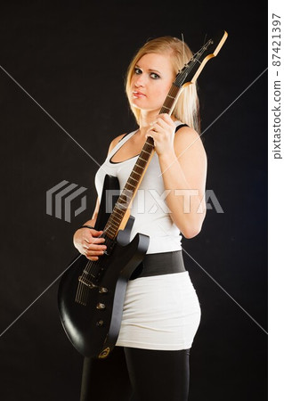Blonde woman holding electric guitar, black background 87421397