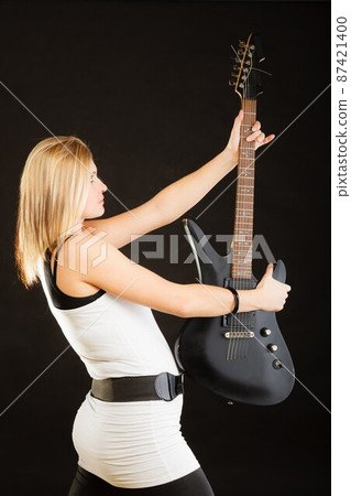 Blonde woman holding electric guitar, black background 87421400