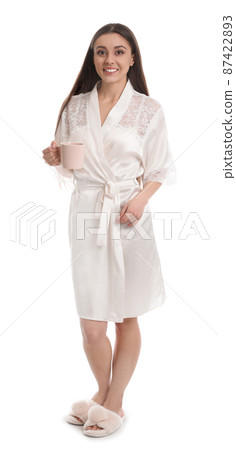Young woman in silk robe with cup of beverage on white background Young woman in silk robe with cup of beverage on white background 87422893