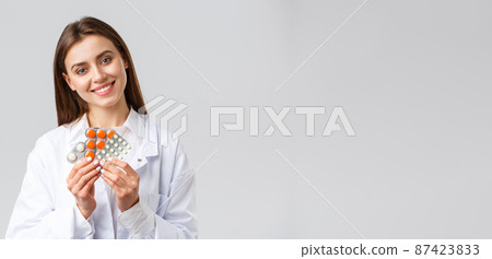 Pharmacy, healthcare workers, insurance and hospitals concept. Gorgeous doctor in white scrubs, female physician or pharmacist smiling, showing medicine, different pills or antibiotics 87423833