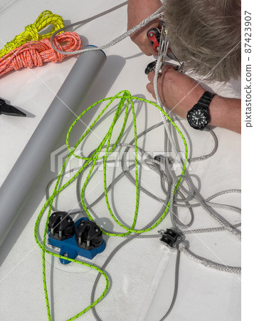 Close-up view of a sailor sets up a sports boat, set of ship equipment, ropes for management of the sailboat of different color, pulleys and ropes, yachting sport, rollers, levers, carbines 87423907