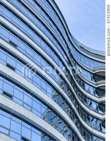 Curved lines of the facade of a large building, reflection of the blue sky in the glass walls, conceptual design Curved lines of the facade of a large building, reflection of the blue sky in the glass walls, conceptual design 87423908