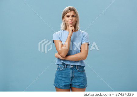 I doubt it good idea. Suspicious intense creative young female coworker in outdoor outfit frowning from doubtful thoughts holding hand on chin while thinking expressing disbelief over blue wall I doubt it good idea. Suspicious intense creative young female coworker in outdoor outfit frowning from doubtful thoughts holding hand on chin while thinking expressing disbelief over blue wall 87424329