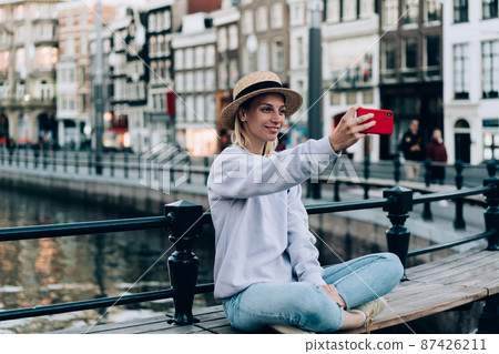 Cheerful woman taking selfie on bench during trip Cheerful woman taking selfie on bench during trip 87426211