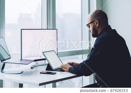 Focused broker typing on tablet keyboard while analyzing graphic Focused broker typing on tablet keyboard while analyzing graphic 87426353