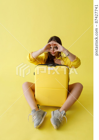 Charming young woman with travel suitcase doing heart sign 87427741
