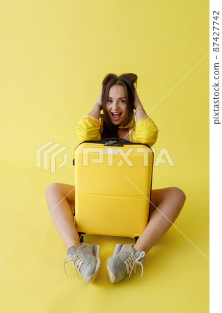 Joyful woman with trolley luggage bag posing in studio 87427742