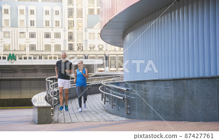 Active middle aged couple in sportswear jogging together in the city in the morning Active middle aged couple in sportswear jogging together in the city in the morning 87427761