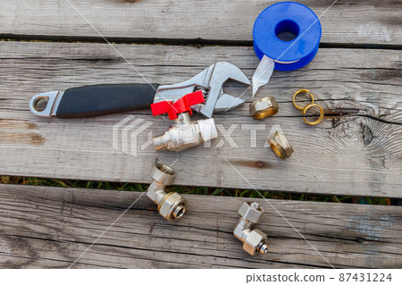 Various plumbing spare parts, sealing tape and adjustable wrench on rustic wooden background. Top view 87431224