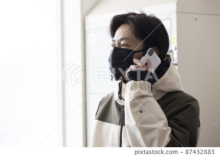 A man in clothing making a phone call in the locker room of a ski resort 87432883
