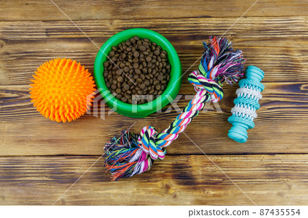 Dog toys and feed for dogs in green plastic bowl on wooden background. Top view. Dog care concept 87435554