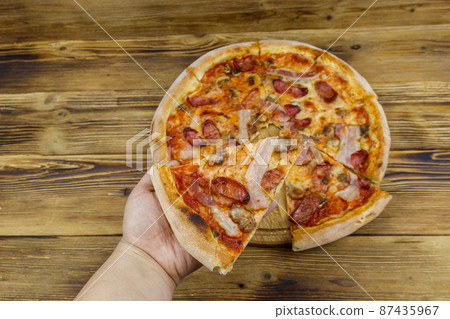 Hand taking a slice of tasty pizza. Hot italian pizza on wooden table. Top view Hand taking a slice of tasty pizza. Hot italian pizza on wooden table. Top view 87435967