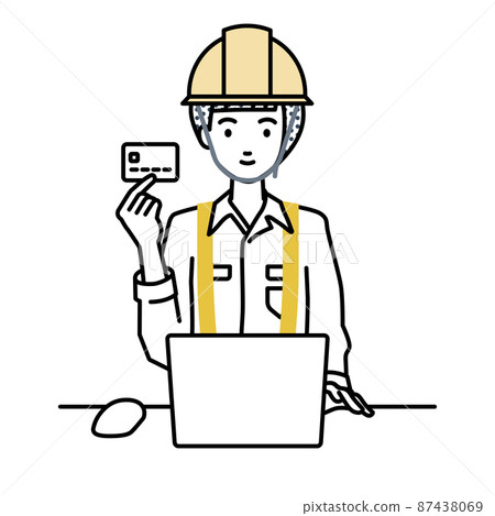 A woman at a construction site sitting at a desk and using a PC while holding a credit card 87438069