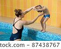 Toddler child learning to dive in indoor swimming pool with teacher. Standing on side, balancing and general physical activity for kids in water, early development. Boy kid instructed 87438767
