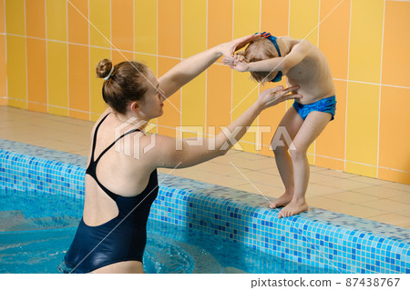 Toddler child learning to dive in indoor swimming pool with teacher. Standing on side, balancing and general physical activity for kids in water, early development. Boy kid instructed Toddler child learning to dive in indoor swimming pool with teacher. Standing on side, balancing and general physical activity for kids in water, early development. Boy kid instructed 87438767
