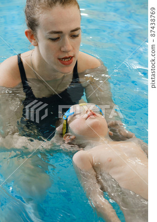 Toddler child learning to swim in indoor swimming pool with teacher. Floating in the water, balancing and general physical activity for kids, early development. Boy kid trained to kick legs and float Toddler child learning to swim in indoor swimming pool with teacher. Floating in the water, balancing and general physical activity for kids, early development. Boy kid trained to kick legs and float 87438769