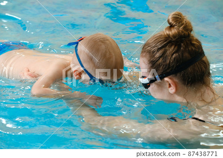 Toddler child learning to dive in indoor swimming pool with teacher. Standing on side, balancing and general physical activity for kids in water, early development. Boy kid instructed Toddler child learning to dive in indoor swimming pool with teacher. Standing on side, balancing and general physical activity for kids in water, early development. Boy kid instructed 87438771