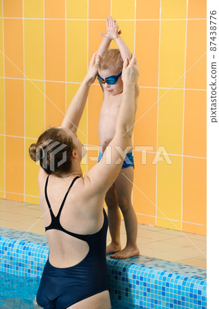 Toddler child learning to dive in indoor swimming pool with teacher. Standing on side, balancing and general physical activity for kids in water, early development. Boy kid instructed Toddler child learning to dive in indoor swimming pool with teacher. Standing on side, balancing and general physical activity for kids in water, early development. Boy kid instructed 87438776