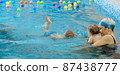 Toddler child learning to swim in indoor swimming pool with teacher. and general physical activity for kids, early development. Boy kid trained to kick legs. Group with instructor in water 87438777