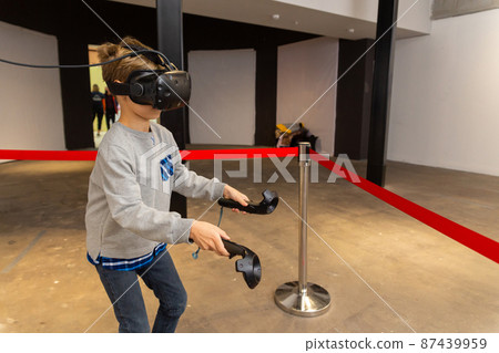 Eight years boy wearing VR headset, holding controllers in hands and enjoying new experience in video game. 87439959