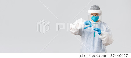 Covid-19, medical research, diagnosis, healthcare workers and quarantine concept. Serious doctor in personal protective equipment, respirator, creating coronavirus vaccine, pouring it in test-tube Covid-19, medical research, diagnosis, healthcare workers and quarantine concept. Serious doctor in personal protective equipment, respirator, creating coronavirus vaccine, pouring it in test-tube 87440407