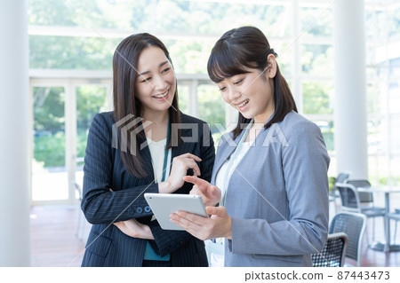 Business Two business women having a conversation while looking at a tablet Business Two business women having a conversation while looking at a tablet 87443473