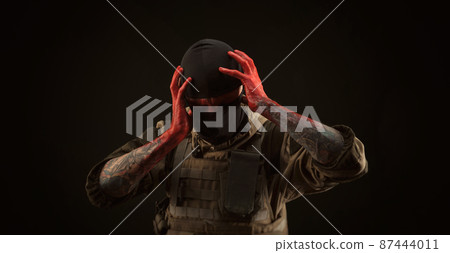 photo of a man in a military uniform and balaclava with a bloody face and hands up to the elbow in blood on a black background photo of a man in a military uniform and balaclava with a bloody face and hands up to the elbow in blood on a black background 87444011