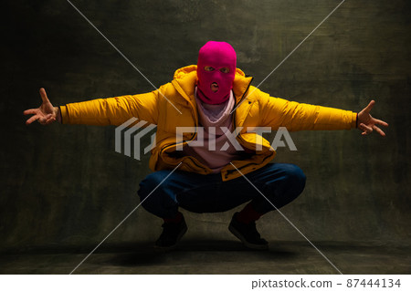 Studio shot of young anonymous man wearing pink balaclava and yellow down jacket, coat isolated on dark vintage background. Concept of safety, art, fashion 87444134