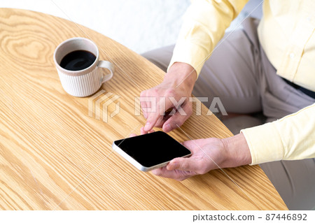 Hands of a middle-aged man who uses a smartphone on a wood table [Parts cut] 87446892