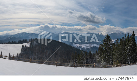 Winter remote alpine mountain village outskirts, countryside hills, groves and farmlands. 87447674