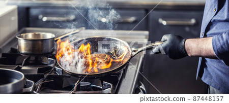 Chef in the kitchen leans pan to the side for alcohol in it to catch fire for gas stove, starting to flambe the food 87448157