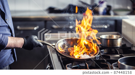 Chef holding pan performing flambe on a dish in it 87448158