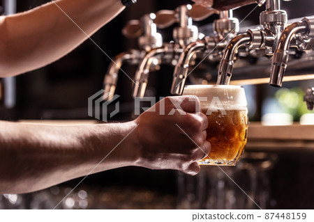 Woman hands of the pub employee tapping beer into a rounded mug. 87448159