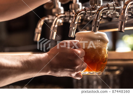 Hand holding mug of beer filled from the tap with foam floating out of the glass 87448160
