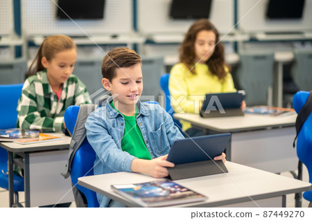 Boy and girls sitting at desk looking at tablet 87449270