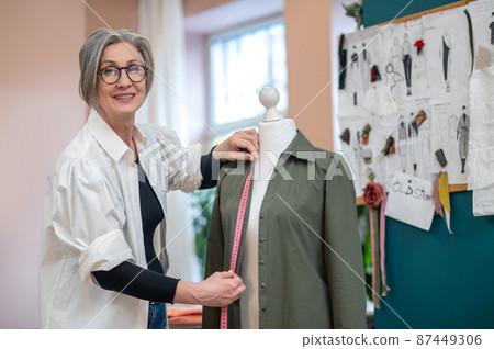 Woman measuring shirt on mannequin looking at camera 87449306