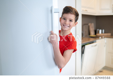 Happy boy looking out of the open fridge door 87449388