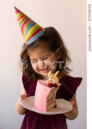 Portrait of pretty birthday girl toddler holding cake with candle. 87450039