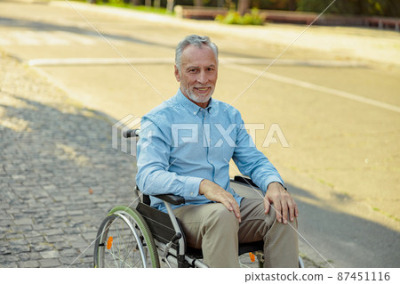 Elderly man in wheelchair smiling at camera while riding alone in the park on a summer day 87451116