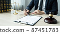 Counselor lawyer or notary working on a documents and report of the important case and wooden gavel, brass scale on table in courtroom 87451783