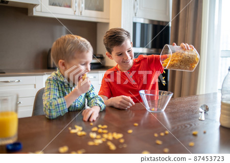 Child observing his cheerful brother preparing breakfast 87453723