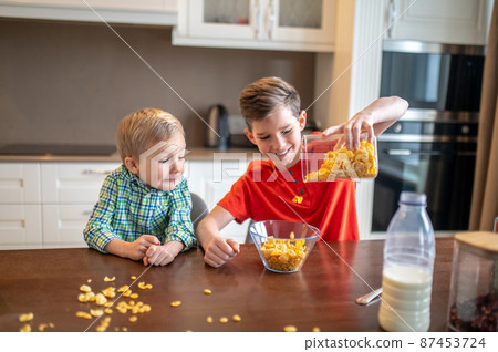 Kid watching his sibling making breakfast in the kitchen Kid watching his sibling making breakfast in the kitchen 87453724