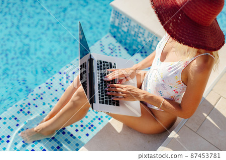 woman using laptop and work remotely near swimming pool 87453781