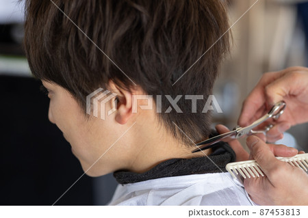 A man who has a haircut in a barber shop 87453813