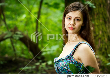 Beautiful young woman wearing elegant white dress walking on a forest path with rays of sunlight beaming through the leaves of the trees 87454055