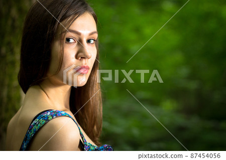 Beautiful young woman wearing elegant white dress walking on a forest path with rays of sunlight beaming through the leaves of the trees Beautiful young woman wearing elegant white dress walking on a forest path with rays of sunlight beaming through the leaves of the trees 87454056