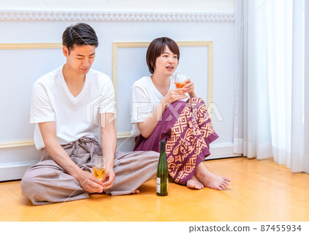 A couple sitting on the floor and tilting the glass A couple sitting on the floor and tilting the glass 87455934