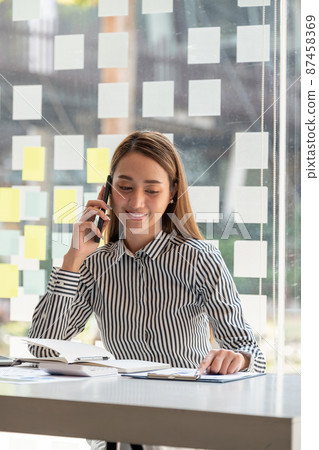 Smiling asian business woman analyst chart financial report and call banker for consult - Financial Concept 87458369