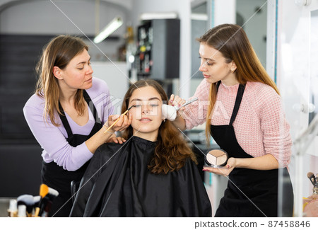 Two makeup artists apply makeup on the face of a young woman 87458846